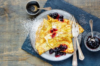 Ahşap masada yabanmersini reçelli haşhaşhaşlı krep.