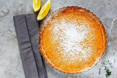 Açık arkaplanda krema serpiştirilmiş limonlu turta.