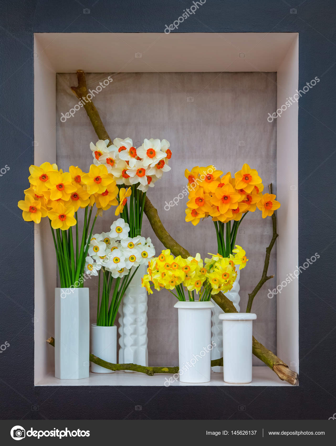 Colorato mazzo di narcisi in vasi bianchi stanno in una cornice in bianco e nero sullo sfondo di un muro di mattoni sotto un panno