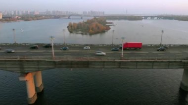 Red truck rides on a road bridge over a river.