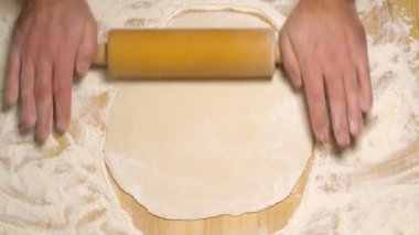 Erkek elleri hamuru ahşap masaya yuvarlıyor, yakın.