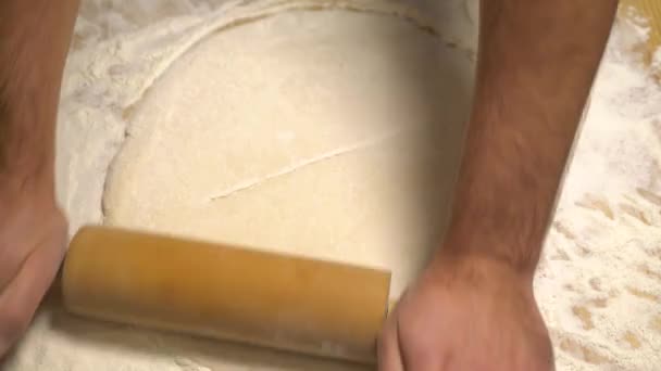 Чоловічі руки розкачують тісто на дерев'яному столі — стокове відео