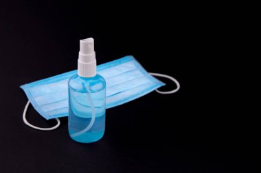 Siyah arka planda tıbbi maske ve dezenfektan. Siyah arka planda antiseptik ve koruyucu tek kullanımlık maske. Hijyen konsepti. Mikropların ve bakterilerin yayılmasını önle ve koronavirüsün bulaşmasını önle.