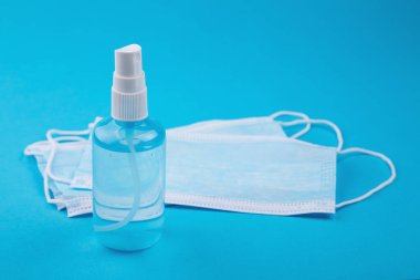 Bir şişe el dezenfektanı, antimikrobik sıvı sprey, mikrop önleme veya antibakteriyel hijyen. Tıbbi maske, mavi arka planda tıbbi koruyucu maskeler. Mavi tıbbi tek kullanımlık yüz maskesi, kapat..