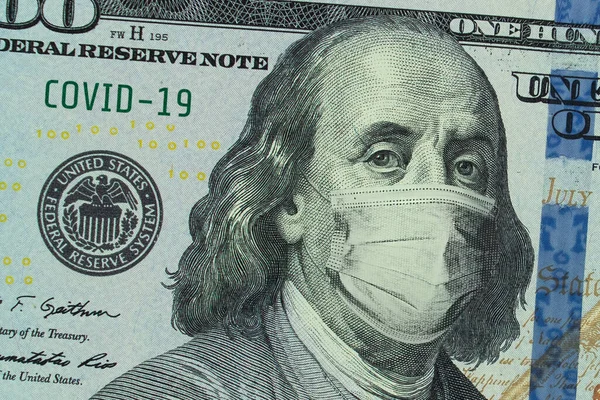 Medical mask on a banknote of 100 dollars, concept of the global financial crisis. Medical mask or surgical mask on american money. COVID-19 coronavirus in USA. Doctor mask protects against COVID-19.