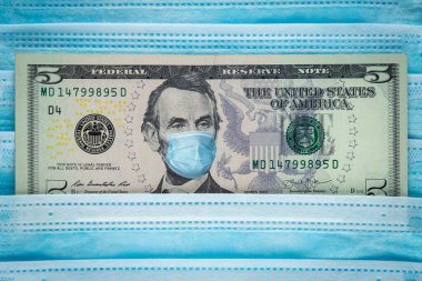 Tıbbi maskeli beş dolarlık banknot. Küresel mali ve ekonomik kriz ABD 'yi etkiledi. Mavi arka planda Coronavirus nedeniyle ABD ekonomisinin çöküşü kavramı, Üst Manzara, yakın plan