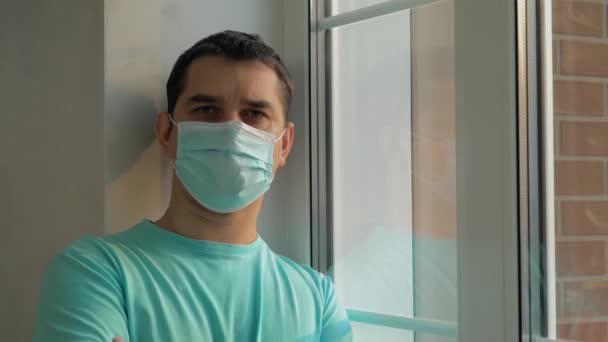 Homem de máscara médica azul olha para a câmera — Vídeo de Stock