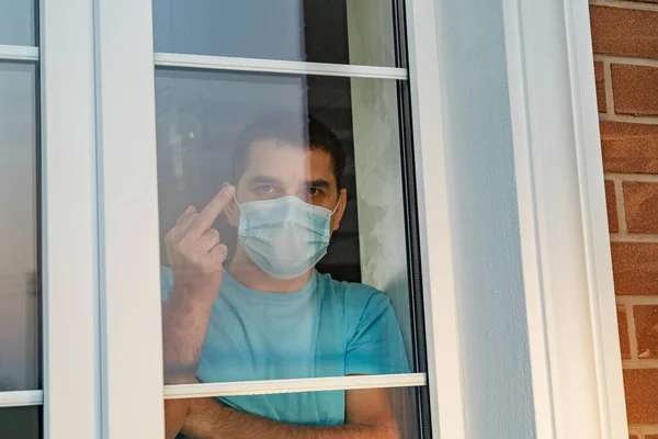 Man in medical mask showing thumbs up sign Fuck. Go away from here. Young angry man with surgical medical mask showing fuck sign at camera. Man tired of quarantine of Coronavirus. Coronovirus pandemic