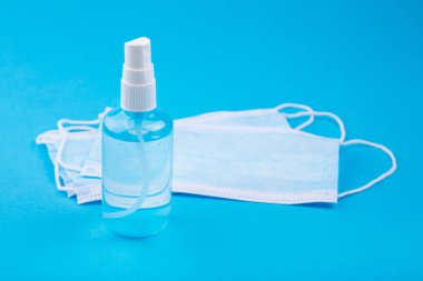 Coronavirus koruyucu ekipman - tıbbi koruyucu maske ve antiseptik dezenfektan spreyi. Mavi arka planda tıbbi maske ve dezenfektan. Coronavirus önleme tıbbi maskeler ve el dezenfektanı spreyi.
