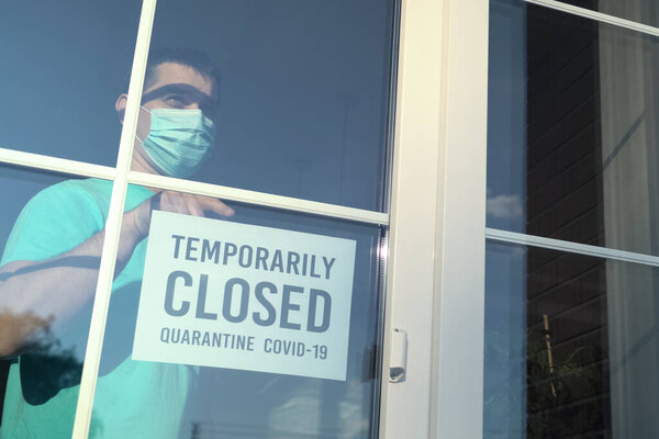 Владелец учреждения клеит табличку с надписью TEMPORALLY CLOSED во время коронавирусной пандемии. Частный бизнес закрывается от пандемии COVID-19. Подпись: Временно закрыт
.