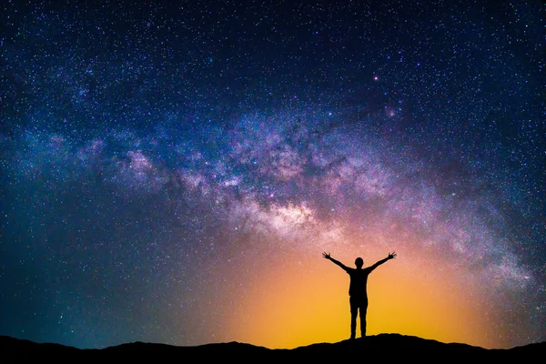 Landscape with Milky way galaxy. Night sky with stars and silhouette happy man on the mountain.