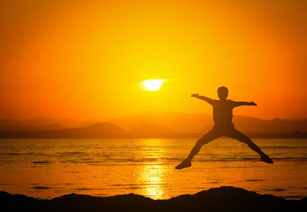 Силуэт прыгуна человека в горах возле пляжа на закате . — стоковое фото