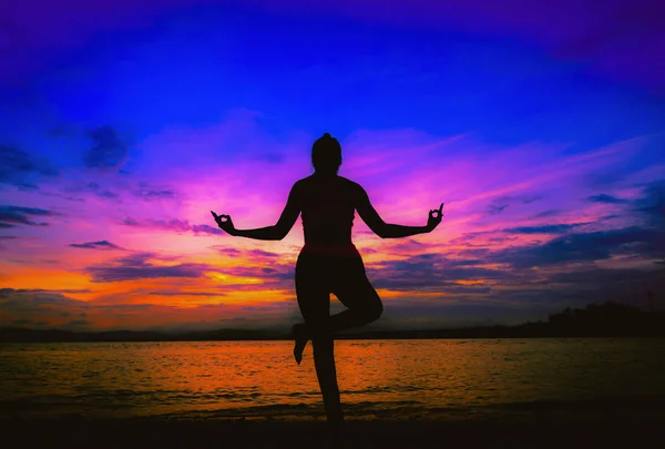 Силуэт молодой женщины практикующей йогу на пляже на закате . — стоковое фото