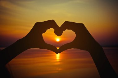 Kalp şeklinde siluet eliyle günbatımı orta ve deniz arka planda