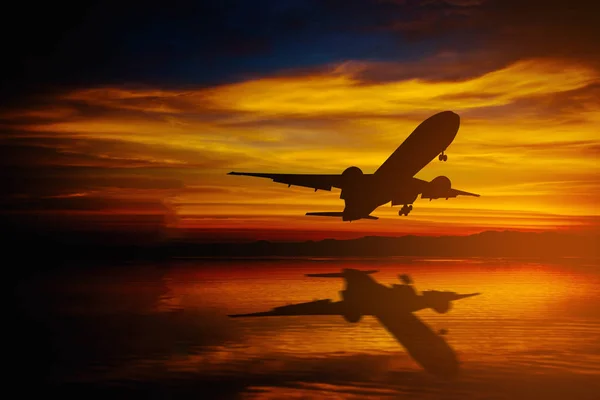 Silueta de avión volar sobre el mar en el cielo dramático durante la puesta del sol . — Foto de Stock