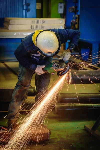 Il lavoratore industriale pesante ha usato la mola elettrica che macina sul tubo d'acciaio nella fabbrica d'acciaio con le scintille . — Foto Stock