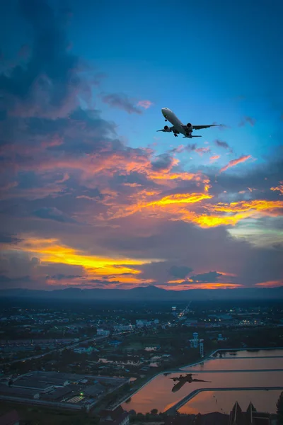 Silueta de avión volar sobre el cielo y la ciudad durante la puesta del sol . — Foto de Stock