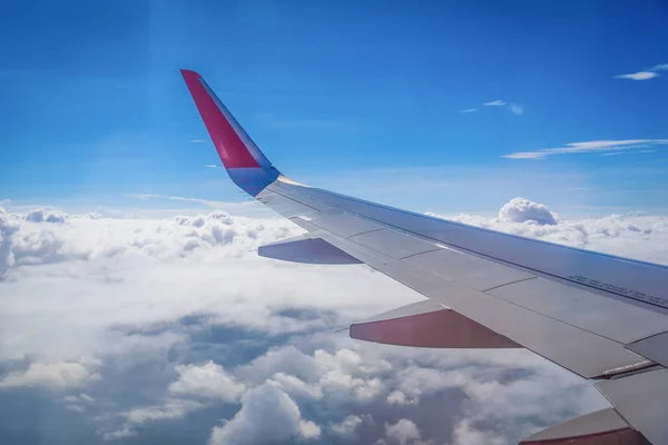 Ala de avión volando por encima de las nubes en el fondo del cielo azul a través de la ventana . — Foto de Stock
