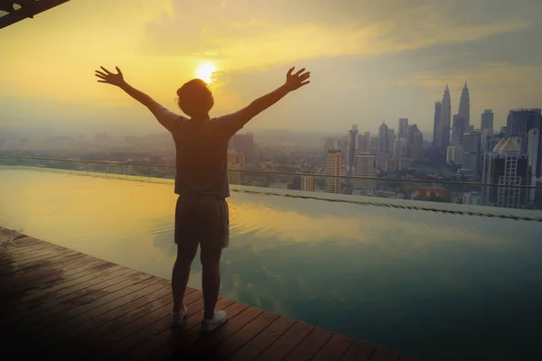 Happy man standing near the swimming pool in roof of hotel at sunrise, Kuala Lumpur, Malaysia . — стоковое фото