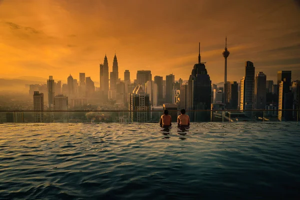 Due viaggiatore uomo in cerca di vista skyline Kuala Lumpur città in piscina sul tetto dell'hotel all'alba a Kuala Lumpur, Malesia . — Foto Stock