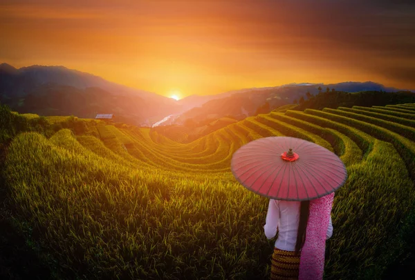 Mulher segurando guarda-chuva vermelho tradicional em campos de arroz com terraço com pavilhão de madeira ao pôr do sol em Mu Cang Chai, YenBai, Vietnã . — Fotografia de Stock