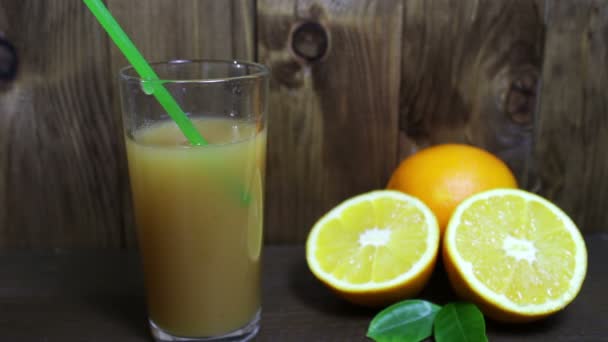Apelsinjuice i ett glas och färsk frukt på trä bakgrund — Stockvideo