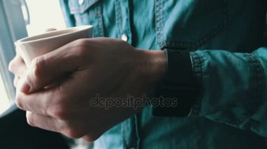 Genç adam beyaz fincan kahve tutan bir akıllı saat kullanarak