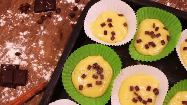 Сырое тесто для кексов в специальной бумажной выпечке, посыпанной кусочками шоколада — стоковое видео