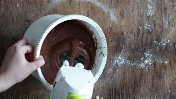 Vista superior revolviendo masa de galletas de chocolate con mezclador eléctrico en un tazón de plástico blanco — Vídeos de Stock