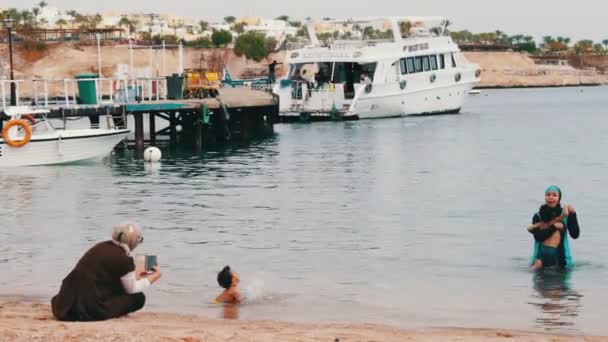 EGITO, SINAI DO SUL, SHARM EL SHEIKH, NOVEMBRO 29, 2016: A família muçulmana banha-se no mar. Uma mulher em hijab com seus filhos nadar no Mar Vermelho . — Vídeo de Stock