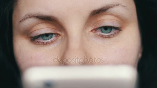 Hermosa chica de ojos verdes se ve en un teléfono inteligente blanco vista de cerca — Vídeos de Stock