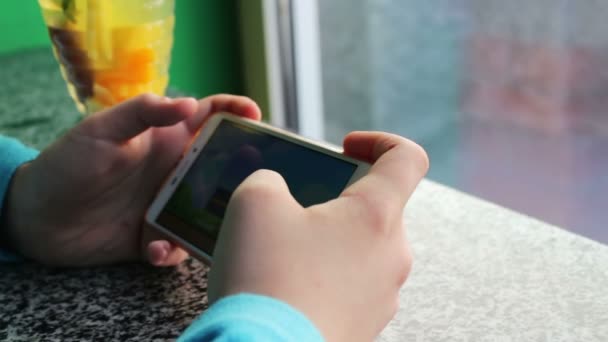 Joven adolescente jugando juego en el teléfono inteligente en la cafetería junto al té de limón con canela — Vídeos de Stock