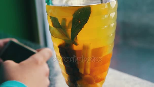 Um menino jogando em um smartphone em um café ao lado de chá de limão com canela — Vídeo de Stock