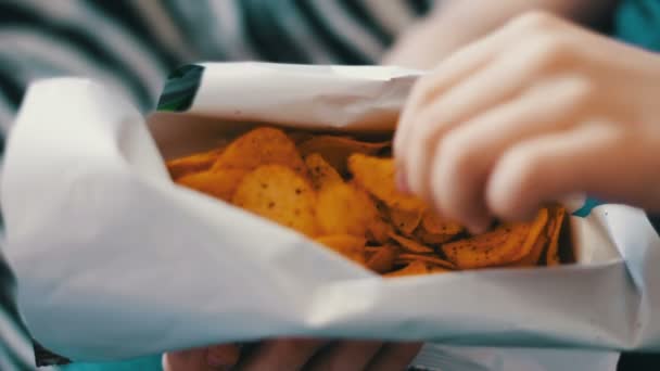 Niño adolescente comiendo papas fritas con las manos en el sofá en casa — Vídeo de stock