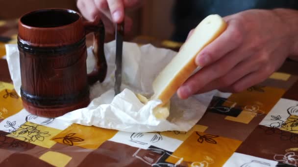 Uomo sta spargendo il burro su un pane accanto a una tazza di caffè caldo — Video Stock