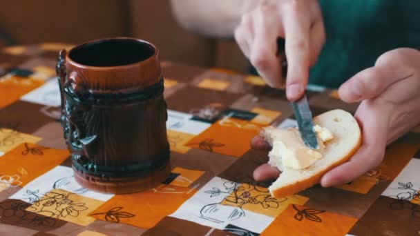 Uomo sta spargendo il burro su un pane accanto a una tazza di caffè caldo — Video Stock