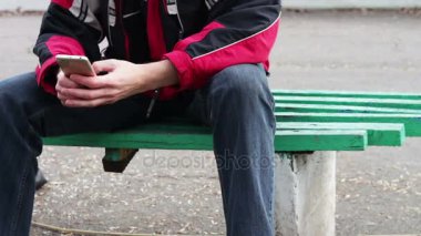 Bir şey üstünde smartphone yazarak bir bankta bir parkta yalnız bir adam oturuyor