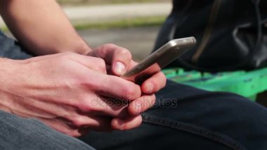 Sokakta, parkta, açık beyaz telefon ile genç adam oturur