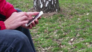 Sokakta, parkta, açık beyaz telefon ile genç adam oturur