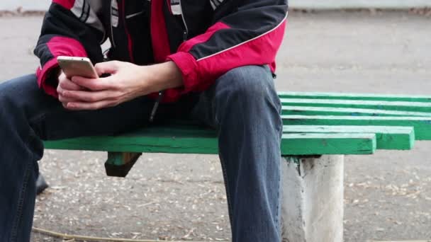 A lonely man sits in a park on a bench typing something on the smartphone — Stock Video