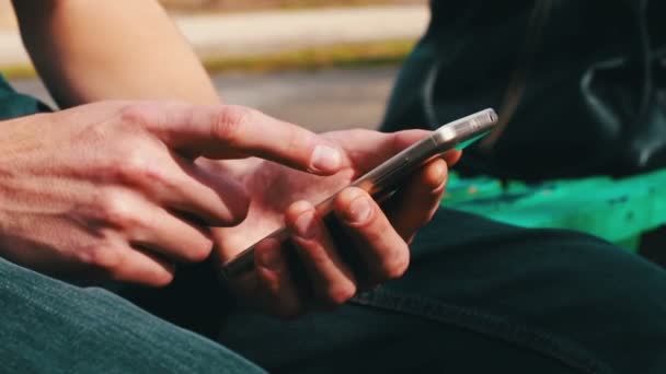 Joven con teléfono blanco se sienta en primavera en la calle, en el parque, al aire libre . — Vídeos de Stock