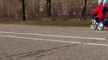 Işık kot pantolon ve ceket genç bir anne bir çocukla mavi bicycle.walking ayakları kaldırım üzerinde yürür.