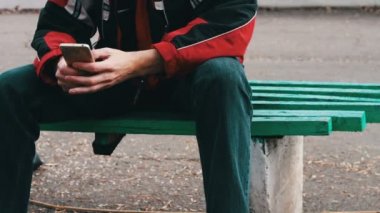 Yalnız bir kırmızı ceket parkta oturan ve bir şey Smartphone'da yazarak