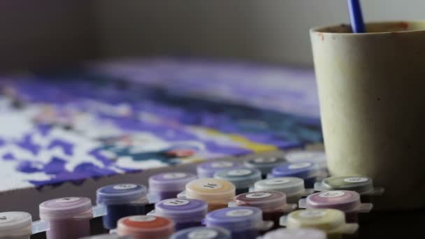 Flickan ritar en bild av siffror, doppa en pensel i ett glas vatten och en burk färg. Färg-Antistress — Stockvideo