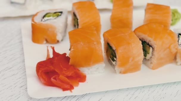 Delicious sushi with salmon, cheese, wasabi, pink ginger, soy sauce on a stylish white wooden background — Stock Video