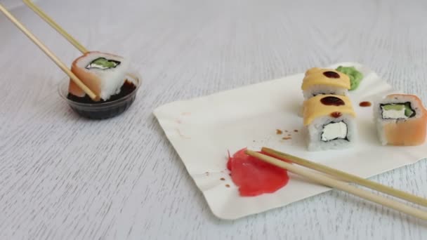 Sushi é tomado com paus chineses e embebido em molho de soja. Sushi delicioso com queijo de gengibre de salmão e wasabi — Vídeo de Stock