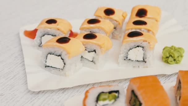 Вкусные суши с лососиной, сыром, васаби, розовым имбирем, соевым соусом на стильном белом деревянном фоне — стоковое видео