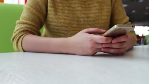 Menina em uma camisola amarela está sentado em um café e algo está digitando em um smartphone — Vídeo de Stock