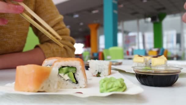 Dziewczyna i facet siedzi w barze sushi i wziąć na kije drewniane sushi — Wideo stockowe