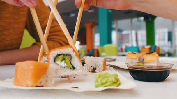 Girl and a guy are sitting in a sushi bar and take with wooden sushi sticks — Stock Video